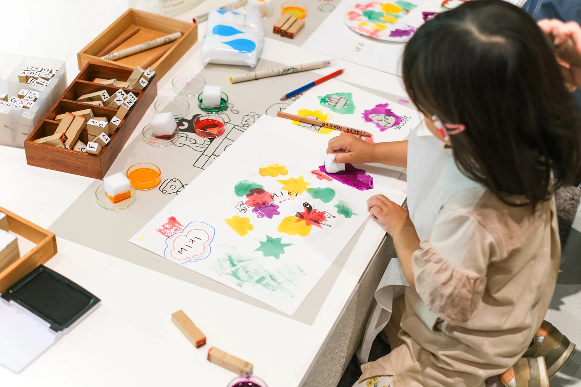 過去のワークショップの様子。小さな子どもが画用紙にさまざまな道具を使って絵を描いている。